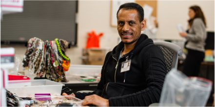 A person sits at a desk surrounded by various jewelry items and crafts